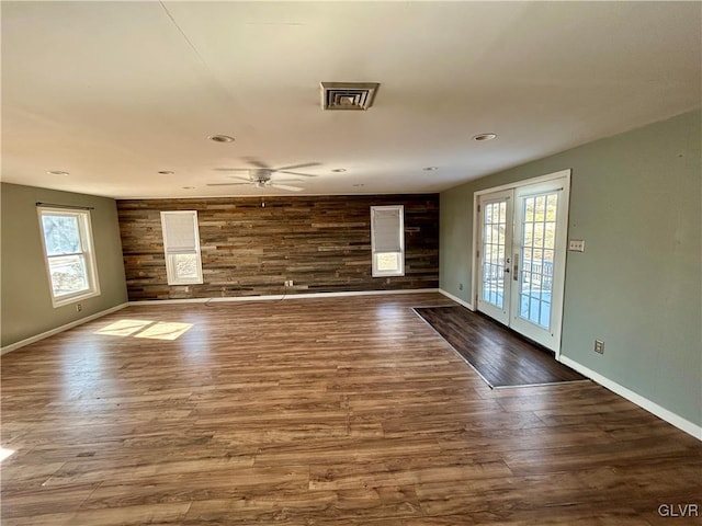 unfurnished living room featuring an accent wall, wood walls, wood finished floors, baseboards, and french doors