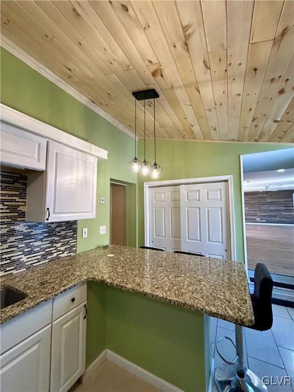 kitchen with stone countertops, white cabinetry, backsplash, and a peninsula