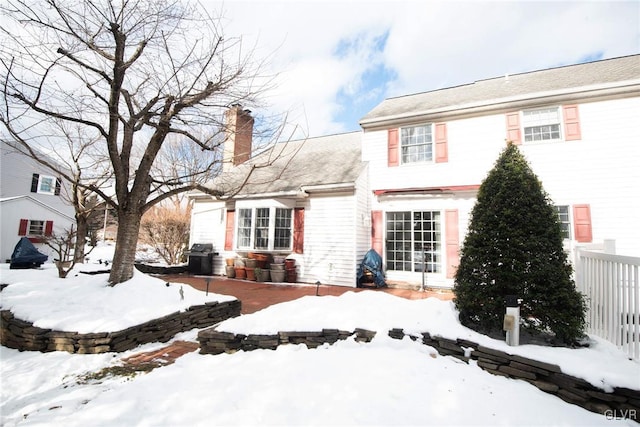 snow covered rear of property with a chimney