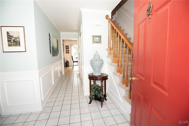 foyer with a wainscoted wall, light tile patterned floors, a decorative wall, stairway, and ornamental molding