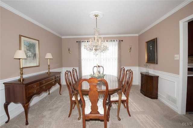 dining space with crown molding, a notable chandelier, visible vents, wainscoting, and light carpet