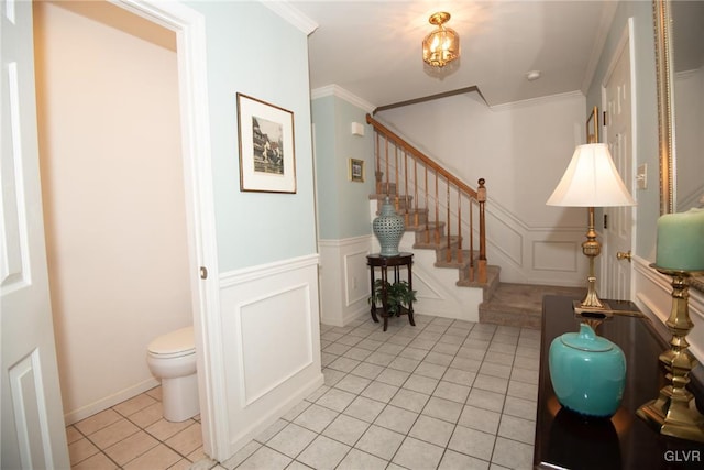 foyer entrance with a wainscoted wall, crown molding, a decorative wall, stairway, and light tile patterned flooring