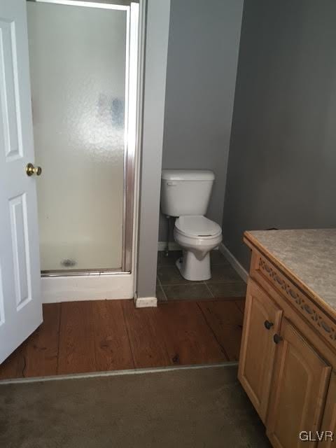 full bathroom featuring baseboards, a shower stall, toilet, and wood finished floors