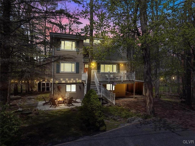 back of house at dusk with a deck, an outdoor fire pit, a patio area, and stairway