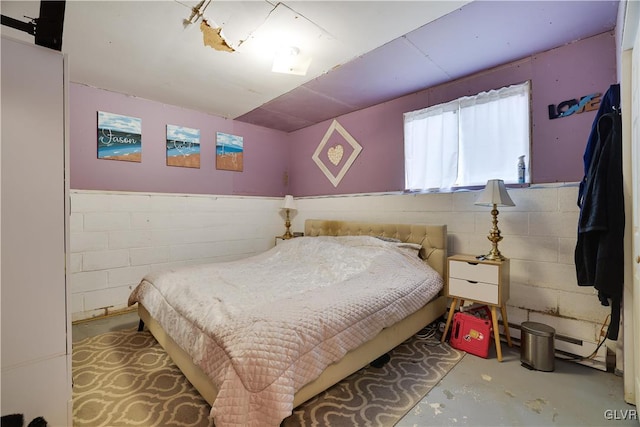 bedroom with concrete block wall, unfinished concrete floors, a baseboard heating unit, and wainscoting