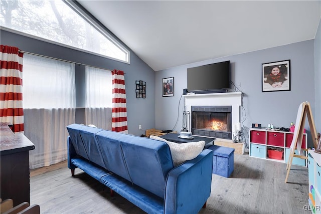living area with a warm lit fireplace, vaulted ceiling, and wood finished floors