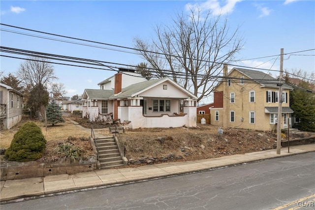 bungalow-style home featuring stairway, a chimney, and stucco siding