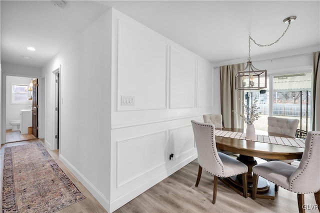 dining area featuring light wood-type flooring, plenty of natural light, baseboards, and a decorative wall