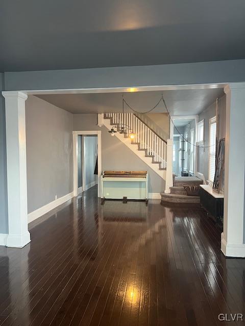 unfurnished living room with baseboards, decorative columns, stairway, and hardwood / wood-style floors