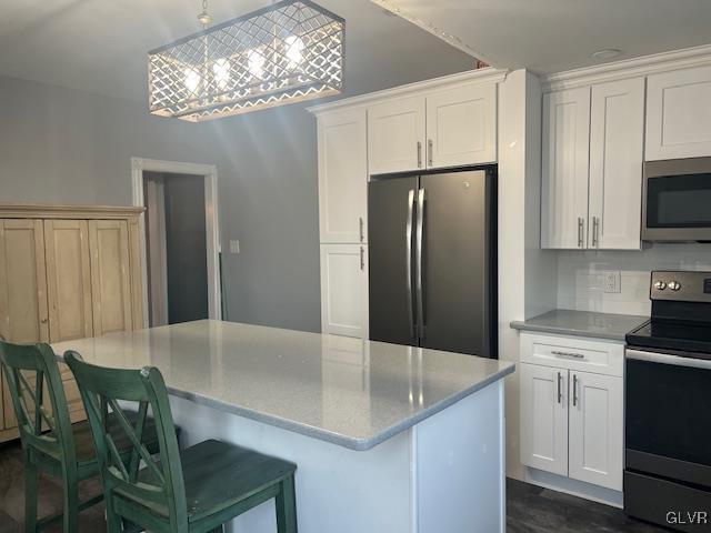 kitchen featuring a center island, a breakfast bar, decorative light fixtures, stainless steel appliances, and white cabinetry