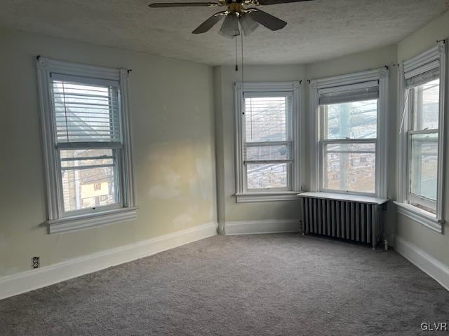 spare room featuring a textured ceiling, ceiling fan, carpet floors, baseboards, and radiator