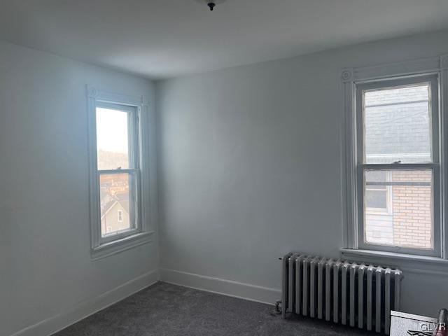 unfurnished room with radiator, dark carpet, and baseboards