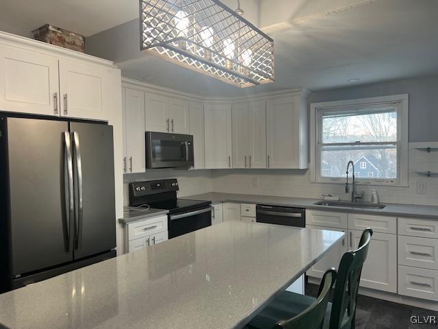 kitchen with a center island, white cabinets, a sink, black appliances, and a kitchen bar