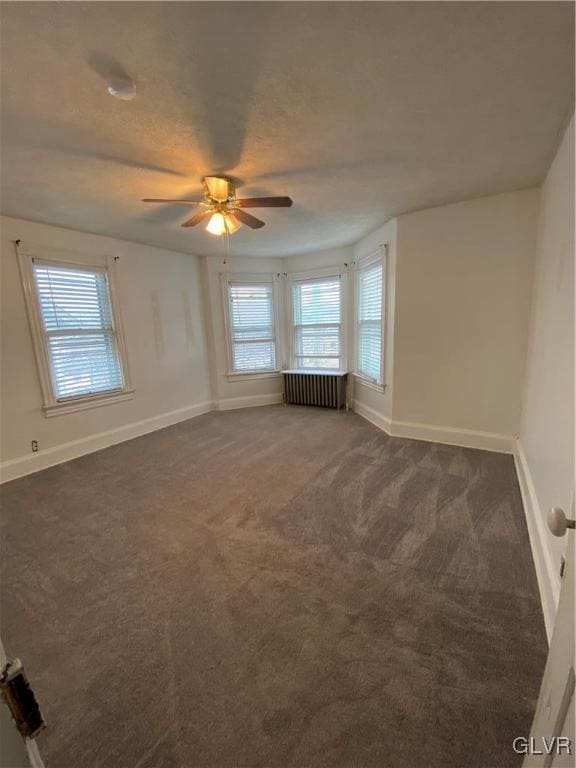 spare room with baseboards, radiator, ceiling fan, a textured ceiling, and dark carpet