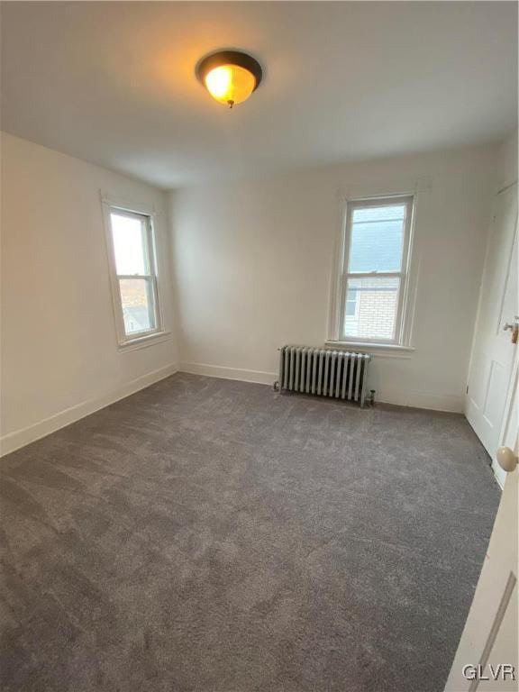 spare room with dark colored carpet, baseboards, and radiator heating unit