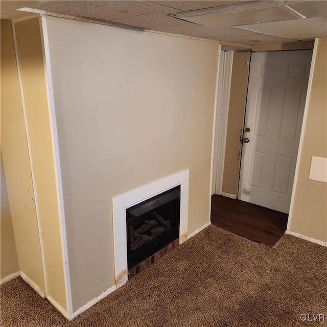 unfurnished living room with carpet, a fireplace, a paneled ceiling, and baseboards