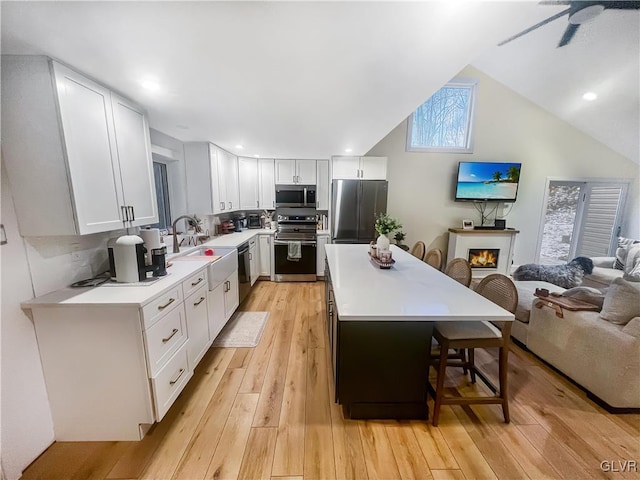 kitchen with stainless steel appliances, light countertops, light wood-style flooring, open floor plan, and a kitchen bar