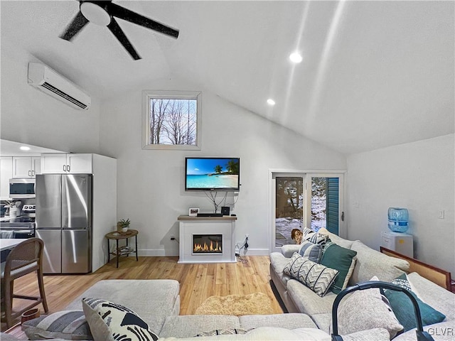 living room featuring a glass covered fireplace, ceiling fan, a wall mounted air conditioner, light wood-style floors, and high vaulted ceiling