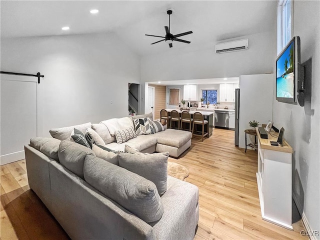 living room featuring a barn door, ceiling fan, an AC wall unit, light wood-type flooring, and recessed lighting