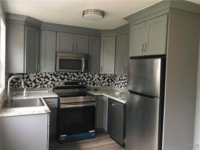 kitchen with stainless steel appliances, gray cabinets, a sink, and decorative backsplash