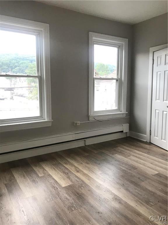 unfurnished room with baseboard heating, plenty of natural light, and wood finished floors