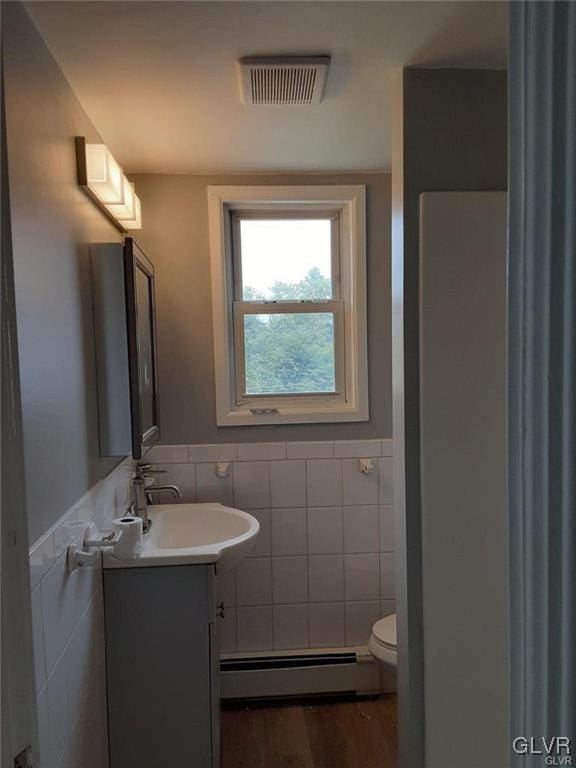 half bath featuring visible vents, toilet, tile walls, and baseboard heating