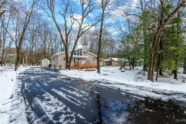 snow covered property featuring a storage shed, a detached garage, and an outbuilding