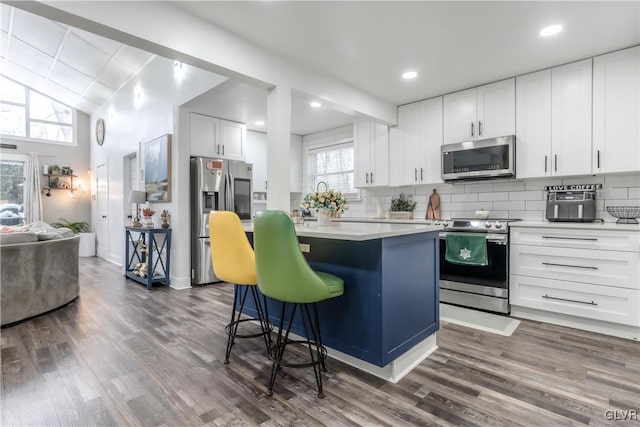 kitchen featuring dark wood-style flooring, light countertops, appliances with stainless steel finishes, backsplash, and a center island