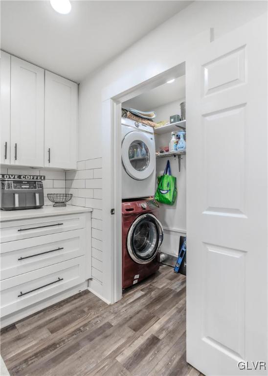 laundry room featuring laundry area, stacked washing maching and dryer, and wood finished floors