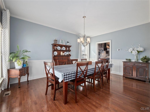 dining space featuring a notable chandelier, dark wood-style flooring, visible vents, wainscoting, and crown molding