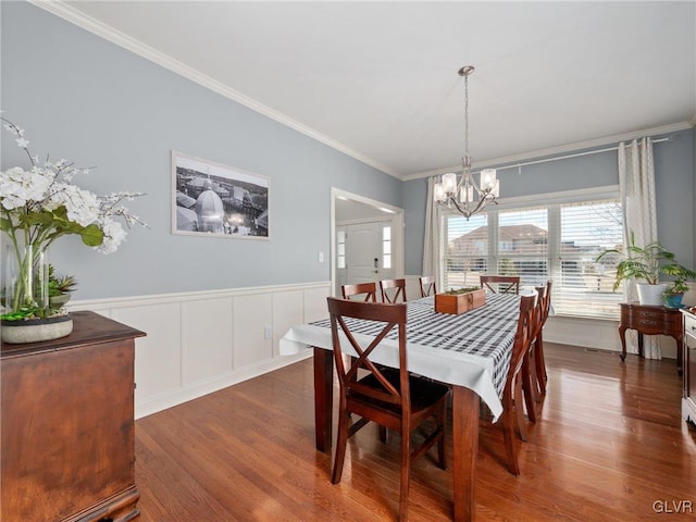 dining area with a wainscoted wall, a notable chandelier, ornamental molding, and wood finished floors