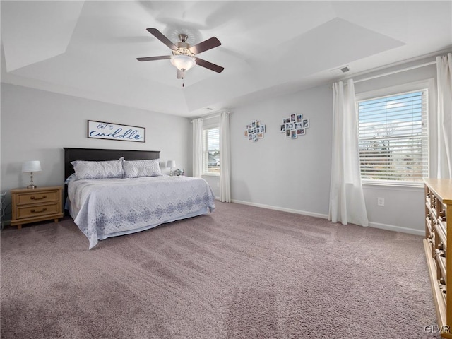 carpeted bedroom featuring a tray ceiling, visible vents, ceiling fan, and baseboards