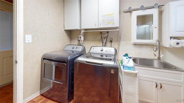 laundry room with light wood-style flooring, independent washer and dryer, a sink, and cabinet space