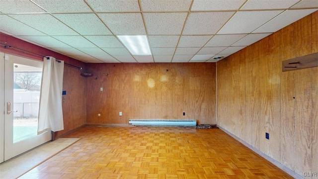 unfurnished room with a paneled ceiling, wood walls, and baseboard heating