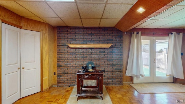 living area with a wood stove, wood walls, a drop ceiling, and french doors