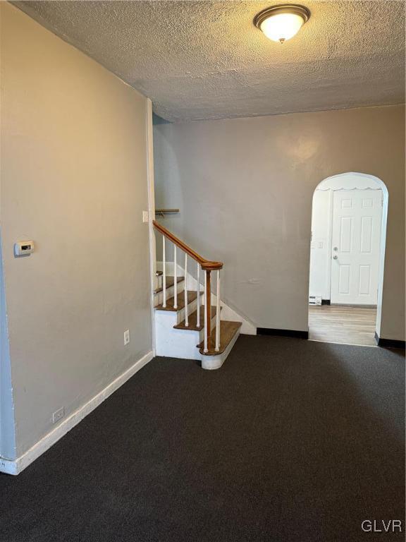 empty room with baseboards, stairway, arched walkways, and a textured ceiling