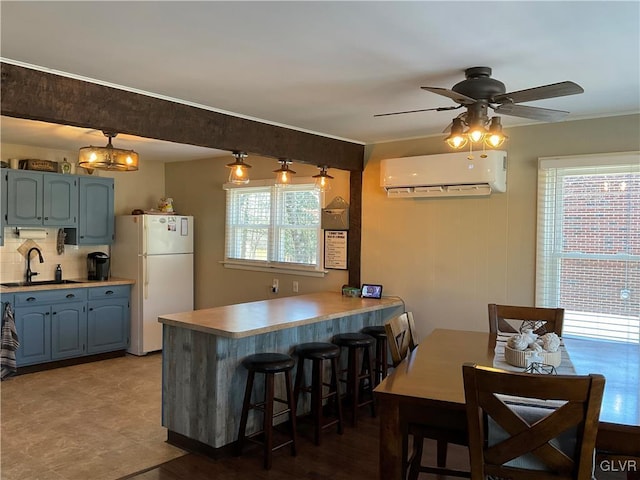 kitchen featuring a peninsula, freestanding refrigerator, a sink, a wall mounted air conditioner, and tasteful backsplash