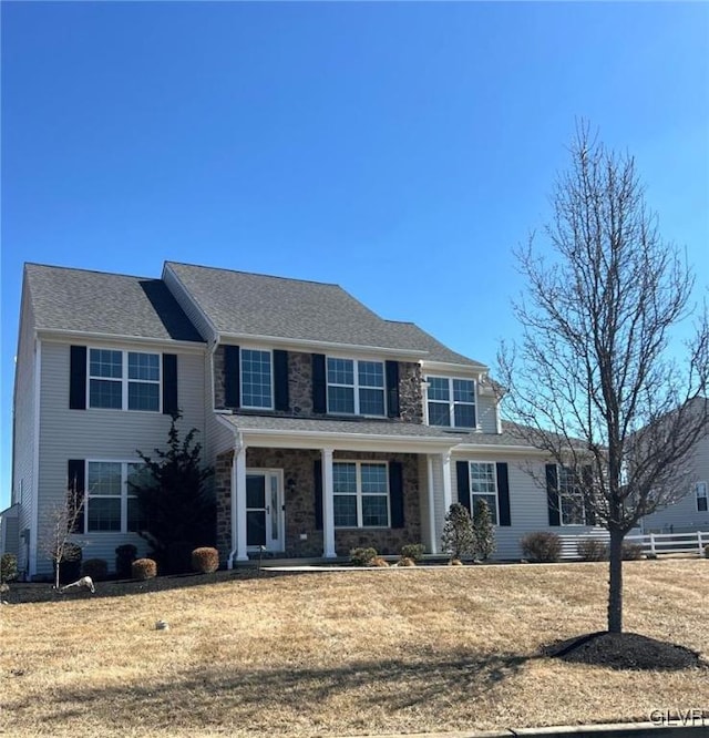 view of front facade featuring stone siding, a front yard, and fence