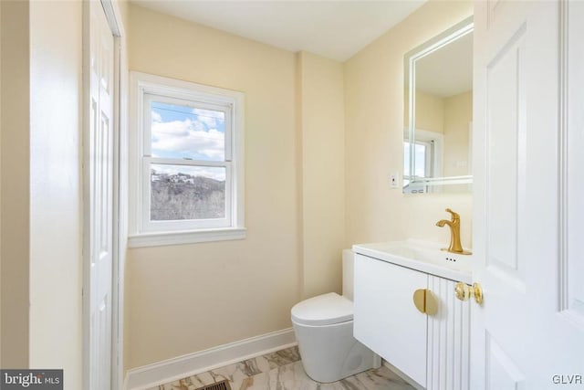 half bathroom with a healthy amount of sunlight, baseboards, toilet, and vanity