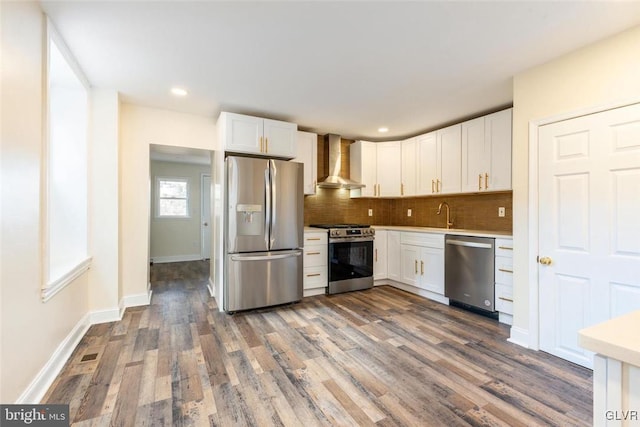 kitchen featuring appliances with stainless steel finishes, wall chimney range hood, white cabinetry, and tasteful backsplash