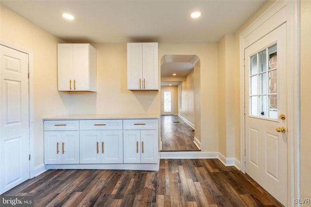 kitchen featuring baseboards, arched walkways, white cabinets, dark wood-style flooring, and recessed lighting