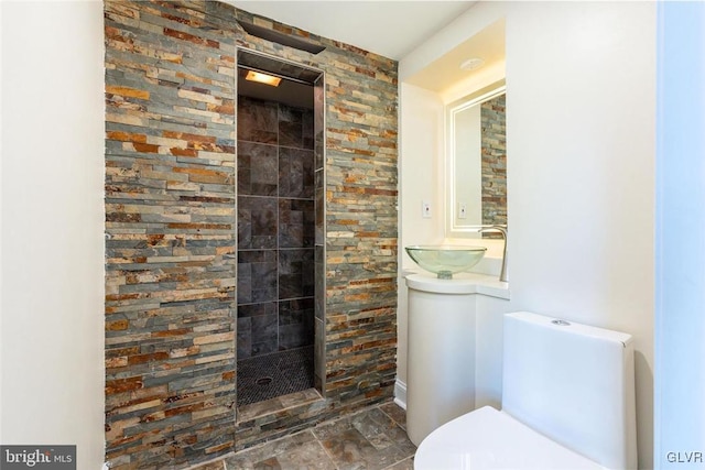 full bath with toilet, stone finish flooring, a walk in shower, and a sink