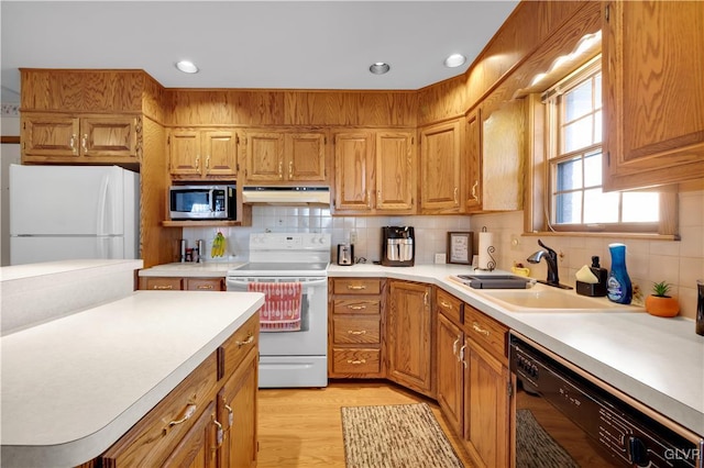 kitchen with white appliances, light wood-style floors, light countertops, under cabinet range hood, and a sink