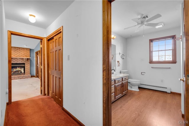 hall with a baseboard radiator, baseboards, light wood-style flooring, and a sink