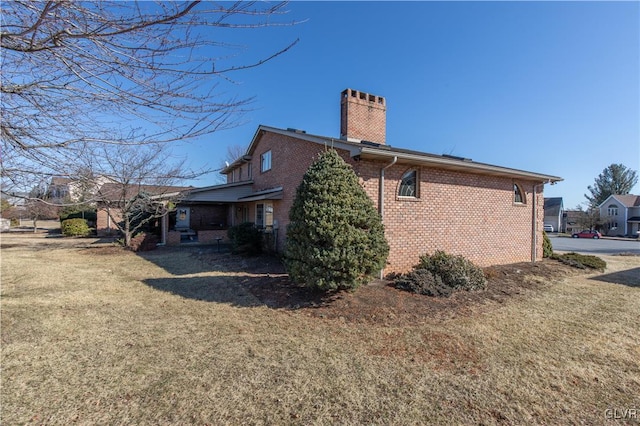 view of side of home with brick siding, a lawn, and a chimney