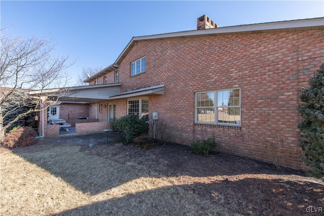 rear view of house featuring brick siding and a chimney