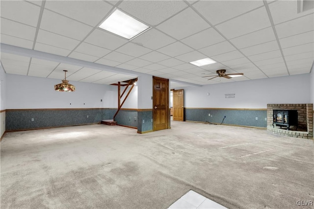 unfurnished living room featuring a wainscoted wall, ceiling fan, a drop ceiling, and carpet flooring