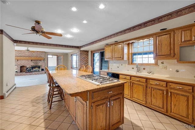 kitchen featuring a kitchen island, baseboard heating, a brick fireplace, stainless steel gas stovetop, and a sink