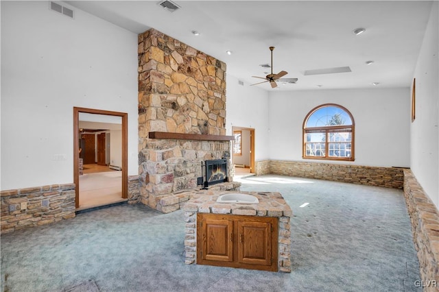 unfurnished living room with a stone fireplace, visible vents, and light carpet