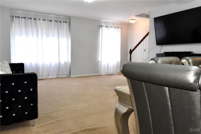 living area featuring light colored carpet, baseboards, and stairs